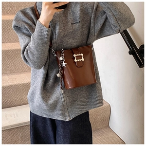 Détail d'un sac seau marron vintage avec un pendentif étoile en métal et des pompons
