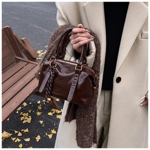 Close-up of deep brown glossy leather bowling bag with gold hardware and knit charm