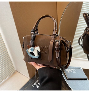 Detailed close-up of dark brown suede Boston bag with embossed lettering and horse charm