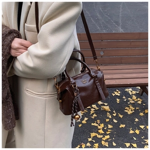 Detail of dark brown leather bowling bag with gold hardware and woven charm