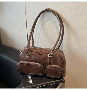 Detail view of dark brown patent leather bowling bag with functional front zip pockets