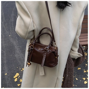 Detail of vintage brown leather bowling bag with gold logo on beige coat scene