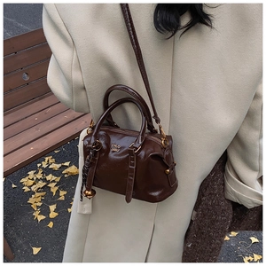 Detail of a dark brown glossy Boston bag with gold logo in an autumn outdoor setting