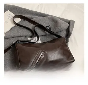 Detail of dark brown leather pillow bag featuring diagonal zipper and round pull tab