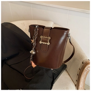 Gros plan d'un sac seau marron foncé avec boucle métallique et pompon tressé