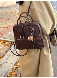 Dettaglio zaino vintage in pelle marrone con ciondolo a hamburger e cerniera intrecciata
