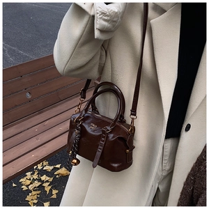 Detail of dark brown polished leather Boston bag with silk scarf on white coat