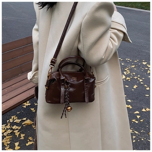 Close-up of deep brown Boston bag with woven bell charm and adjustable shoulder strap