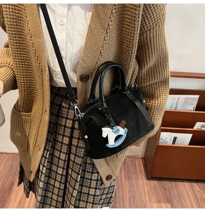 Dettaglio della borsa Boston nera opaca con goffratura di lettere e ciondolo a cavallo