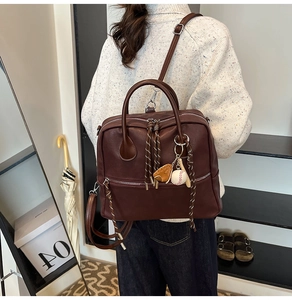 Dettaglio di uno zaino in pelle marrone scuro con ciondolo da baseball e doppia zip