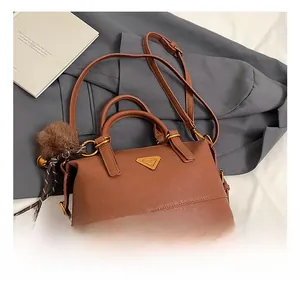 Detail of brown faux leather pillow bag with gold triangle logo and pom-pom charm