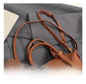 Detail shot of brown leather pillow bag with gold hardware and plush pompom charm