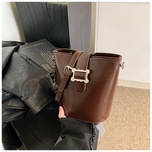 Détail d'un sac seau marron foncé en cuir PU brillant avec boucle en métal doré chic