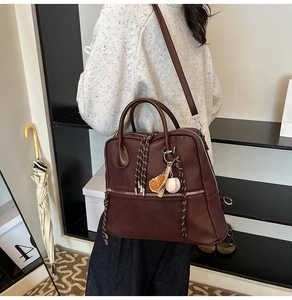 Dettaglio della borsa vintage marrone con tiretti intrecciati e ciondolo da baseball