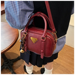 Nahaufnahme der weinroten Retro-Handtasche mit goldenem Dreieckslogo und Glocke