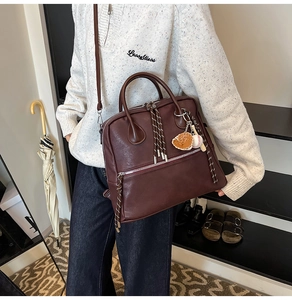 Dettaglio della borsa vintage in pelle marrone con ciondolo baseball e tirazip tessuti