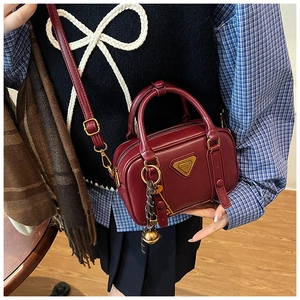 Details einer vintage weinroten Boston-Tasche mit Goldlogo an einem Damenmodell