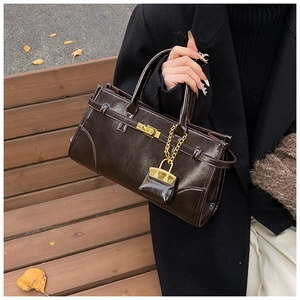 Detail einer glänzenden dunkelbraunen Handtasche mit Goldschloss und Mini-Anhänger