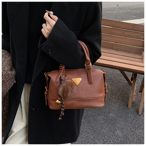 Detail of vintage brown leather pillow bag with fluffy pompom and golden bell charm