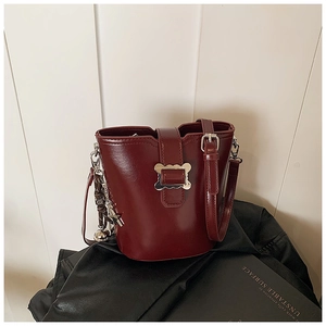 Détail d'un sac seau bordeaux avec boucle dorée sur fond de cuir noir et livre élégant