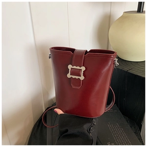Détail du sac seau en cuir bordeaux avec boucle argentée ondulée et texture fine raffinée