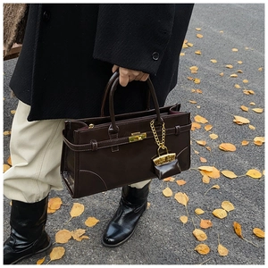 Detail of dark chocolate glossy handbag with gold twist lock on autumn street