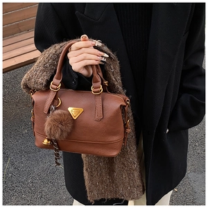 Close-up of brown pillow bag featuring a gold triangle plaque and faux fur pompom charm