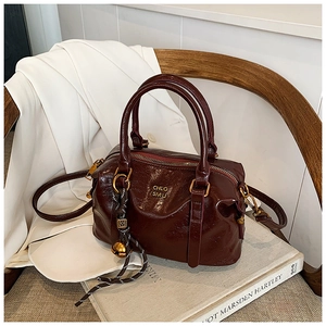 Close-up of deep burgundy glossy leather bag with gold hardware and bell charm