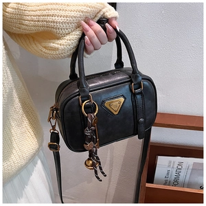 Detail einer schwarzen Boston-Handtasche mit goldenem Dreieckslogo und Web-Anhänger