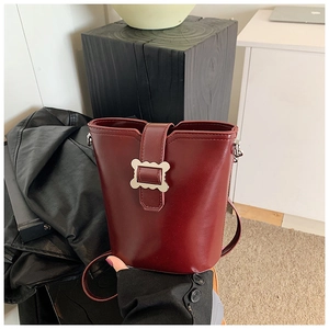 Détail du sac seau bordeaux avec boucle argentée ondulée et texture de cuir lisse