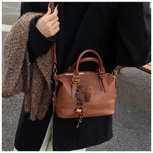 Close-up of brown Boston bag featuring fluffy charm and adjustable leather strap