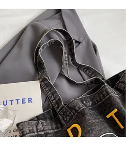 Detailed view of black washed denim tote bag with yellow letter embroidery and wide straps