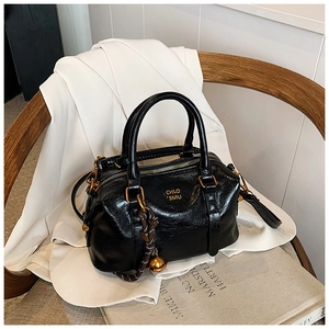 Detail of black glossy leather Boston bag with gold hardware on a wooden chair