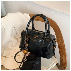 Detail of a black glossy Boston bag with gold logo and stylish charm on white books