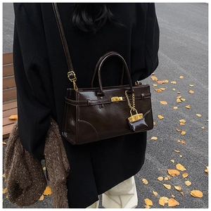 Detail der kaffeebraunen Ledertasche mit goldenem Drehverschluss und Mini-Beutel-Zubehör