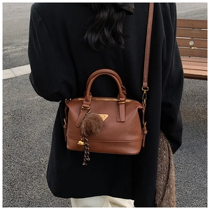Detail of a brown Boston bag with golden triangle logo and faux fur pompom on shoulder strap