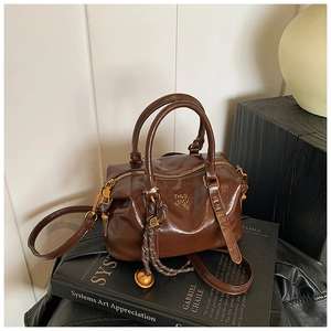 Detail of dark brown leather handbag with gold hardware and braided knot charm on a book