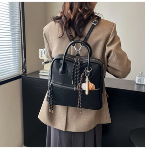 Dettaglio dello zaino nero in ecopelle con ciondolo da baseball e nappe intrecciate ai cursori
