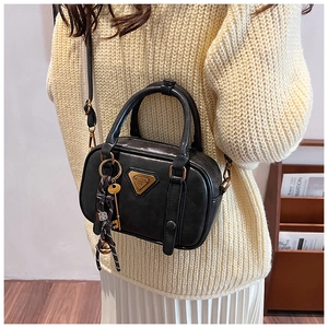 Detail einer schwarzen Handtasche aus Leder mit goldenem Dreieckslogo und Strickpullover