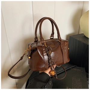 Detailed macro of brown Boston bag showing pleated faux leather and gold bell charm