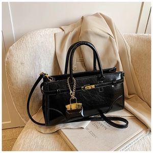 Detail of black embossed leather tote bag with gold buckle and mini pouch on white chair