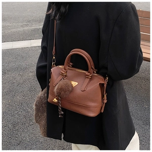 Detail view of deep brown leather Boston bag with plush ball charm on a black coat