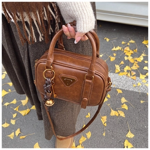 Detailansicht einer braunen Vintage-Handtasche mit goldener Glocke auf Herbstlaub