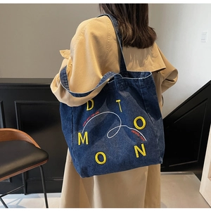 Detail of blue denim tote bag with yellow embroidery and white artistic script