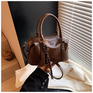 Detailed close-up of brown glossy leather Boston bag with gold logo and woven charm