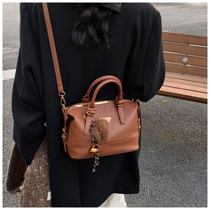 Detail of a brown Boston handbag with fur ball charm and gold hardware on a street model