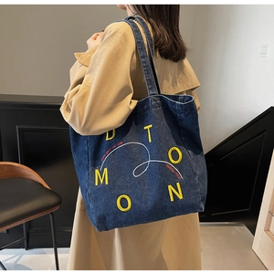 Detail shot of navy denim tote bag with yellow embroidered logo and street style print