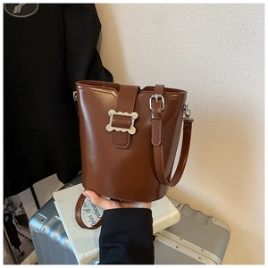 Détail du sac seau en cuir marron brillant avec boucle en métal ondulé et bandoulière réglable