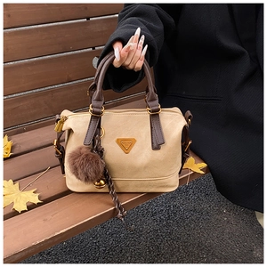 Close-up of khaki suede pillow bag with plush pendant on a wooden autumn bench