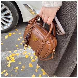 Detailansicht der braunen Retro-Handtasche mit goldener Plakette und Glockenanhänger